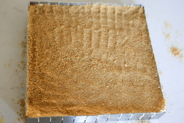 A square metal pan sits on a white counter, packed with a smooth layer of fine graham cracker crumbs—just waiting to become the base for some delicious no-bake Strawberry Shortcake Icebox Bars.
