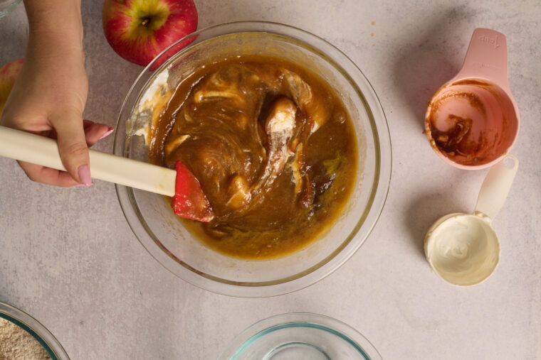 Apple butter and sour cream being folded into the wet ingredients for apple cake.