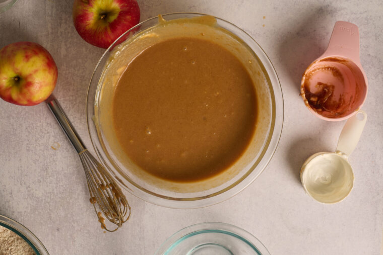 Smooth apple cake wet ingredients whisked together in a glass bowl.