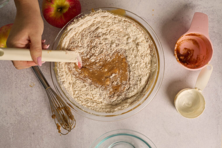 Dry ingredients being folded into the wet apple cake mixture.