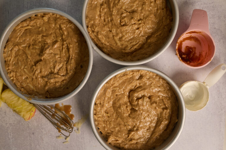 Apple cake batter divided between three round cake pans before baking.