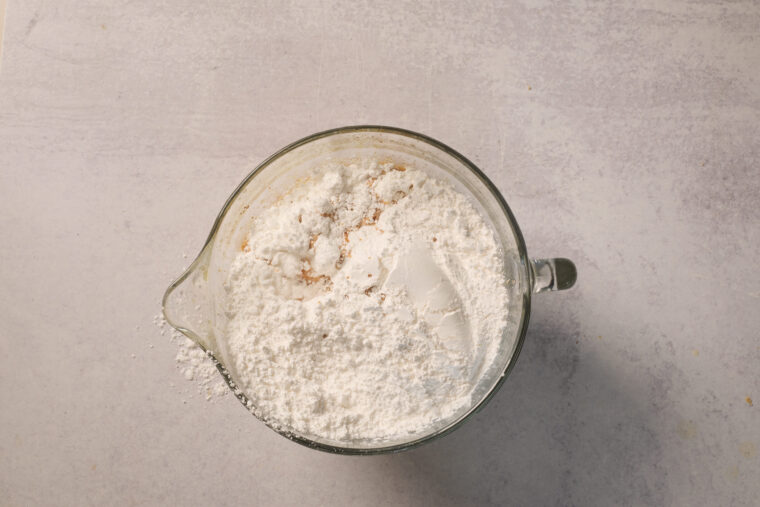 Looking down at a glass bowl with flour and sugar inside, ready to whip up an apple cake on a bright countertop.