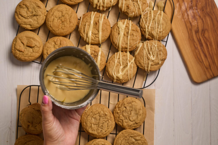 drizzling glaze on maple brown sugar cookies on cooling racks.