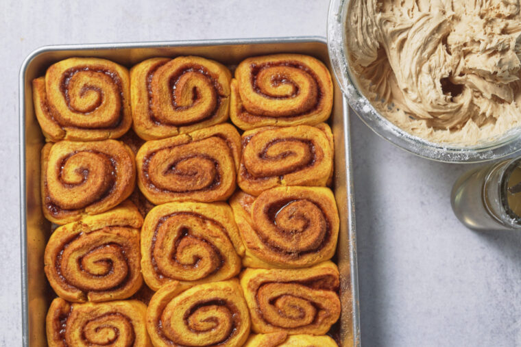 freshly baked pumpkin cinnamon rolls with frosting next to them